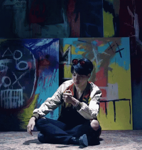 a man is sitting on the floor in front of a wall with a painting of a skull and crossbones