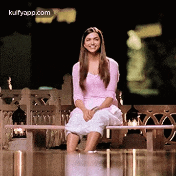 a woman in a pink shirt and white skirt is sitting on a bench and smiling .