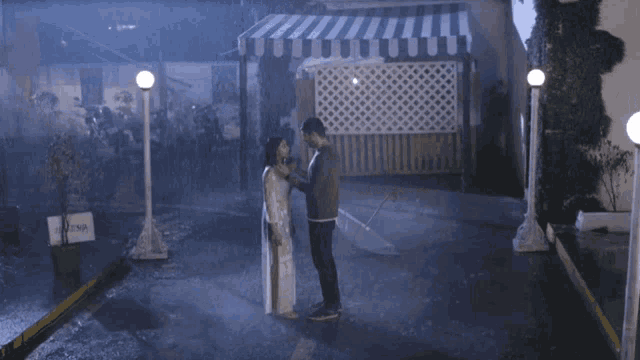 a man and a woman are standing under an umbrella in the rain in front of a sign that says ' india ' on it