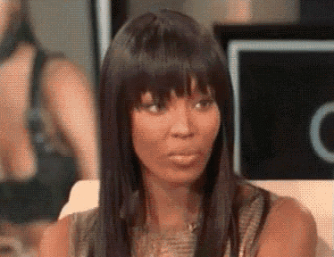 a woman with long hair and bangs is sitting on a couch and making a funny face .
