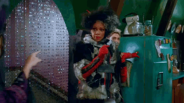 a woman in a fur coat and red gloves is standing next to a refrigerator .