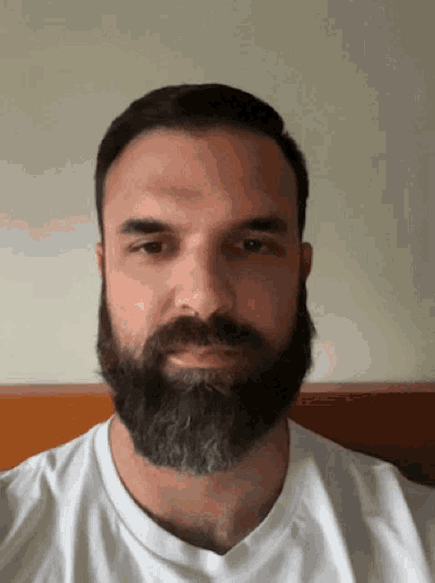 a man with a beard and a white shirt looks at the camera