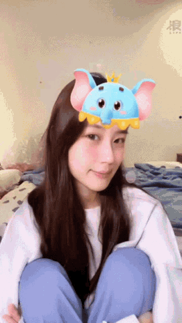a girl wearing a blue elephant headband sits on a bed