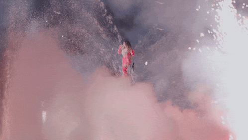 a woman in a pink dress is surrounded by pink smoke