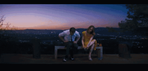 a man and a woman sit on a bench with a view of a city