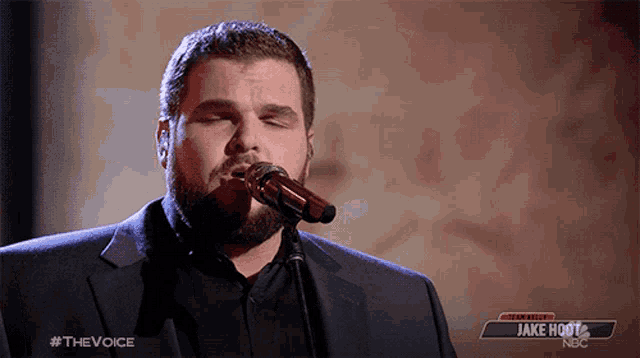 a man singing into a microphone with a nbc logo in the background