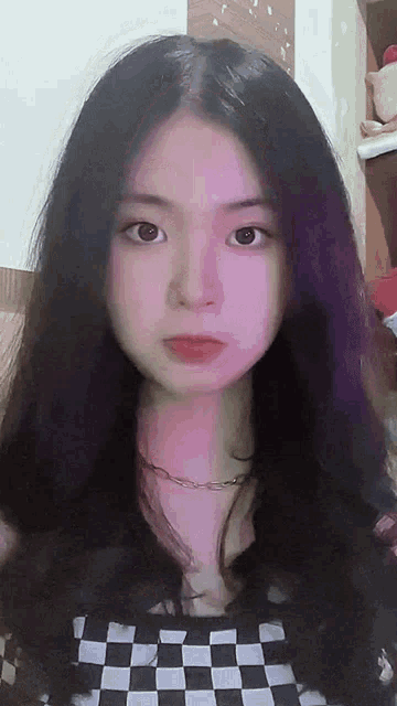 a girl with long black hair and a checkered shirt looks at the camera