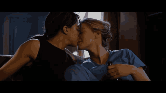 a man and a woman are kissing on a couch and the woman is holding a bottle
