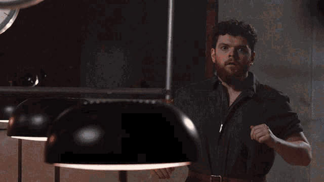 a man with a beard stands in front of a clock with the number 6