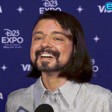 a man with long hair and a beard is smiling in front of a blue backdrop that says disney expo
