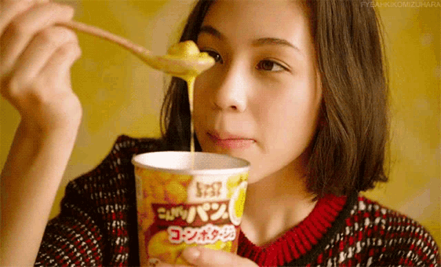 a woman is eating soup from a cup with a spoon in her mouth