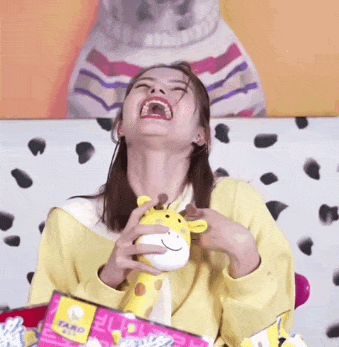 a woman in a yellow sweater is holding a stuffed giraffe