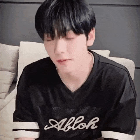 a young man wearing a black shirt is sitting on a couch with his eyes closed and his mouth open .