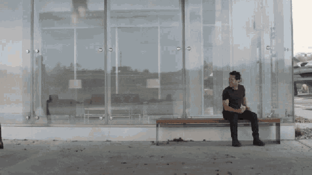 a man sits on a bench in front of a glass wall