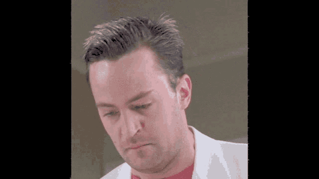 a man wearing a white jacket and a pink shirt looks down