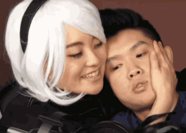 a woman in a wig kisses a man on the forehead