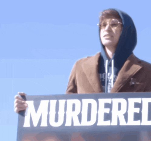 a man holding a sign that says murdered in white letters