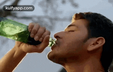 a man is drinking from a green bottle .