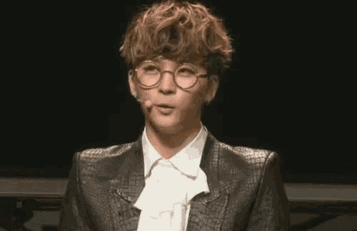 a young man wearing glasses and a bow tie is talking into a microphone .