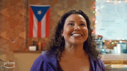 a woman is smiling in front of a flag and a sign that says prime