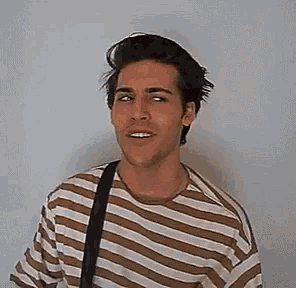 a young man wearing a striped shirt and a black strap is smiling .