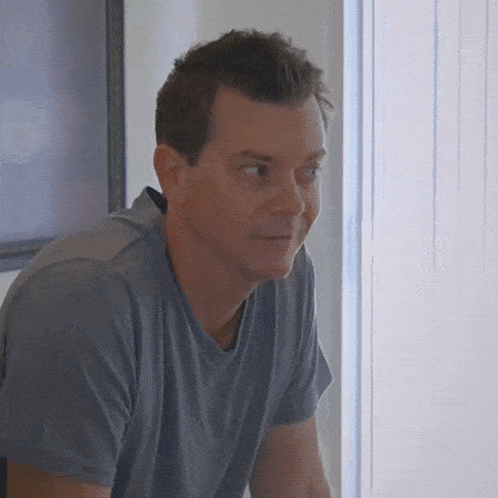 a man in a grey shirt is looking out a window