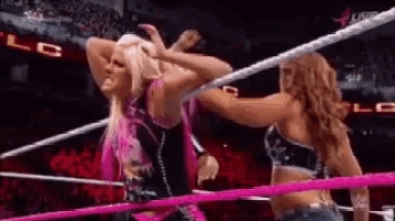 two women are wrestling in a ring with pink ropes and a crowd watching .