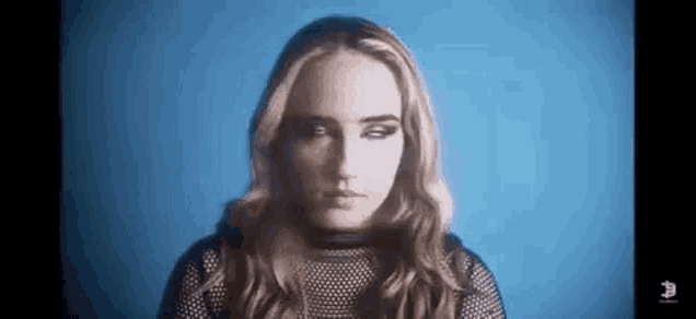 a woman with long hair is standing in front of a blue background and looking at the camera .