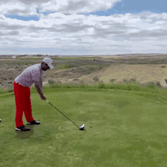 a man in red pants is swinging a golf club on a green