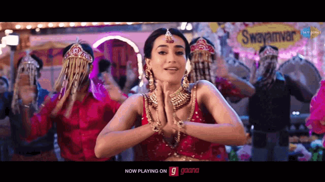 a woman in a red dress is dancing in front of a sign that says swayamvar