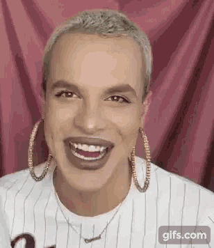 a man wearing hoop earrings and a striped shirt is smiling and making a funny face .