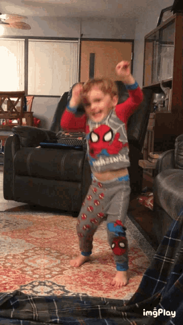 a young boy wearing a spider-man shirt is dancing in a living room