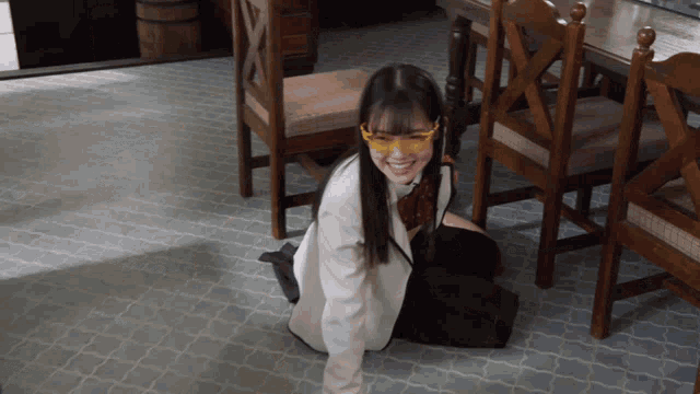 a girl wearing glasses sits on the floor in a room