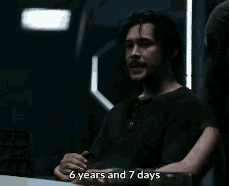 a man in a black shirt is talking to a woman in a dark room and the words 6 years and 7 days are next to him