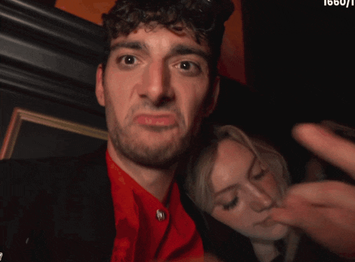 a man in a red shirt is making a funny face next to a woman in a black jacket