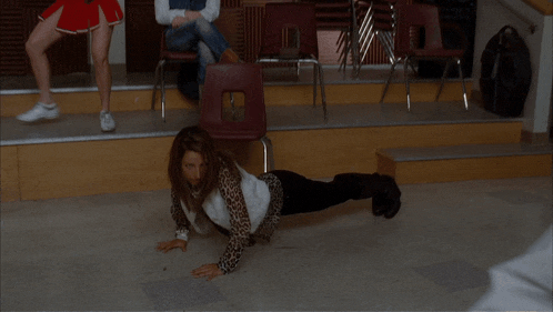 a woman is doing push ups on the floor while a cheerleader watches