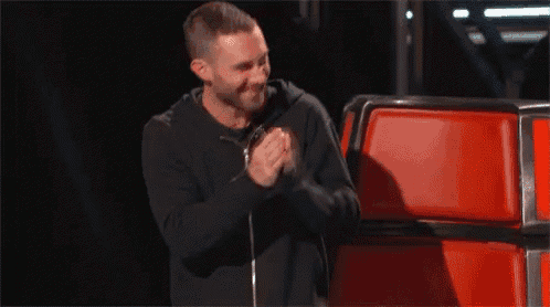 a man is singing into a microphone while standing in front of a red chair .