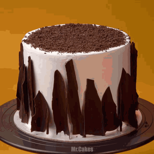 a white cake with chocolate shavings on top and the words mr.cakes on the bottom