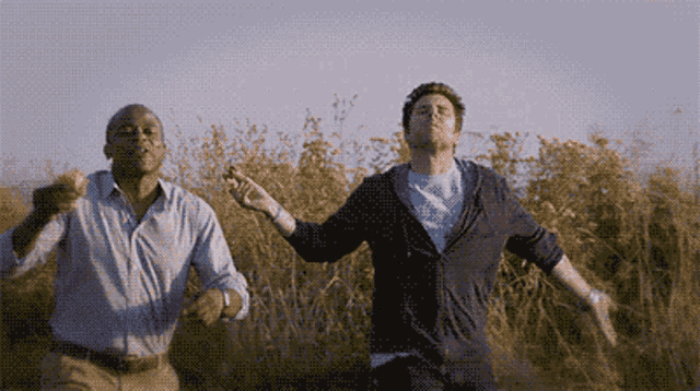 two men are running through a field of tall grass