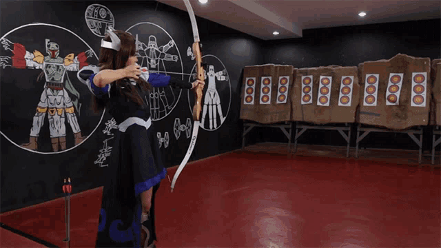 a woman is holding a bow and arrow in front of a wall that has a star wars drawing on it