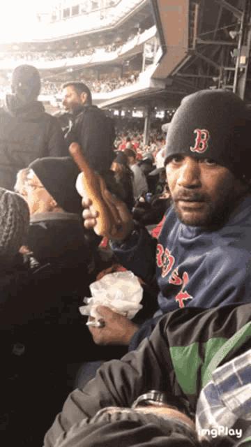 a man wearing a hat with the letter b on it is holding a hot dog