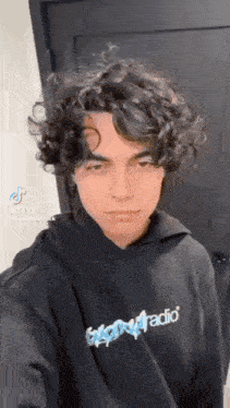 a young man with curly hair is wearing a black hoodie and taking a selfie .