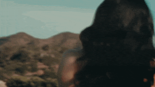 a woman with long black hair is standing in front of a mountain .