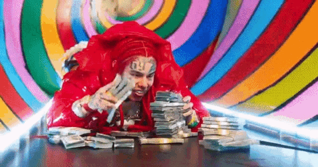 a man in a red jacket is sitting at a table surrounded by a pile of money .