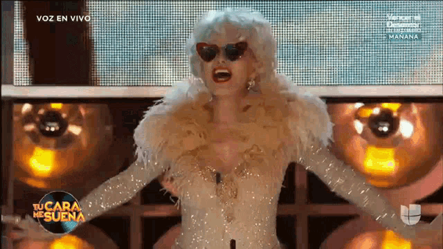 a woman in a feathered dress is on a tv screen with the words voz en vivo on the bottom