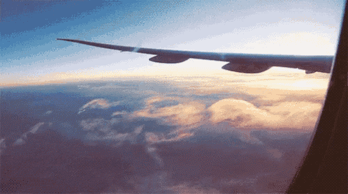 the wing of an airplane flying through the clouds at sunset