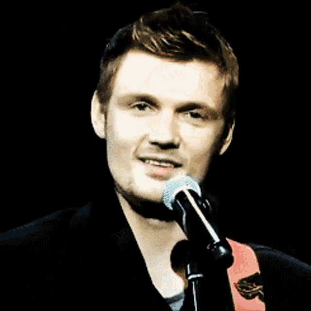 a man singing into a microphone with a guitar strap around his neck
