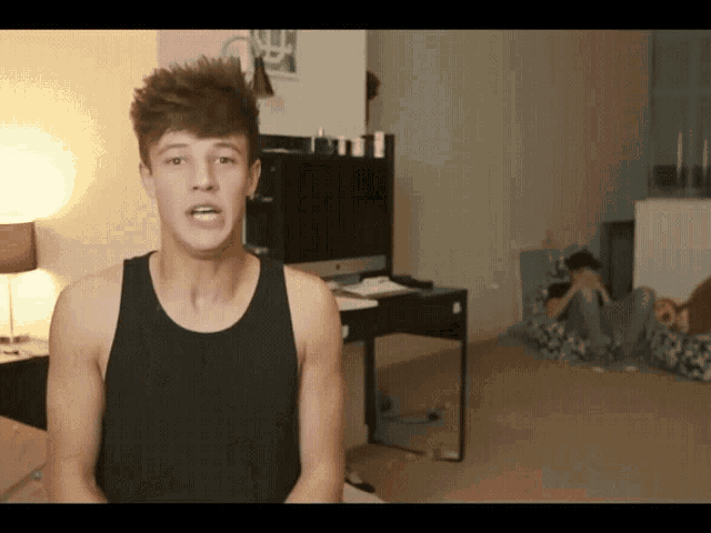 a young man in a black tank top is sitting in a room