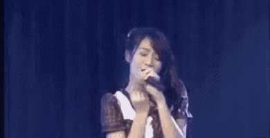 a woman is singing into a microphone while making a heart shape with her hands .