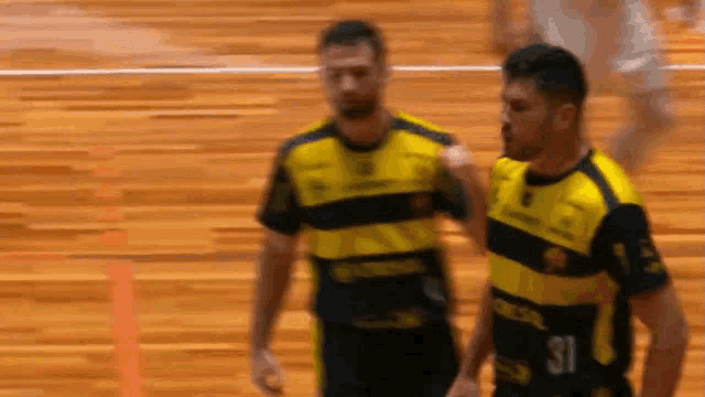 two men are standing on a wooden floor and one has the number 31 on his jersey .